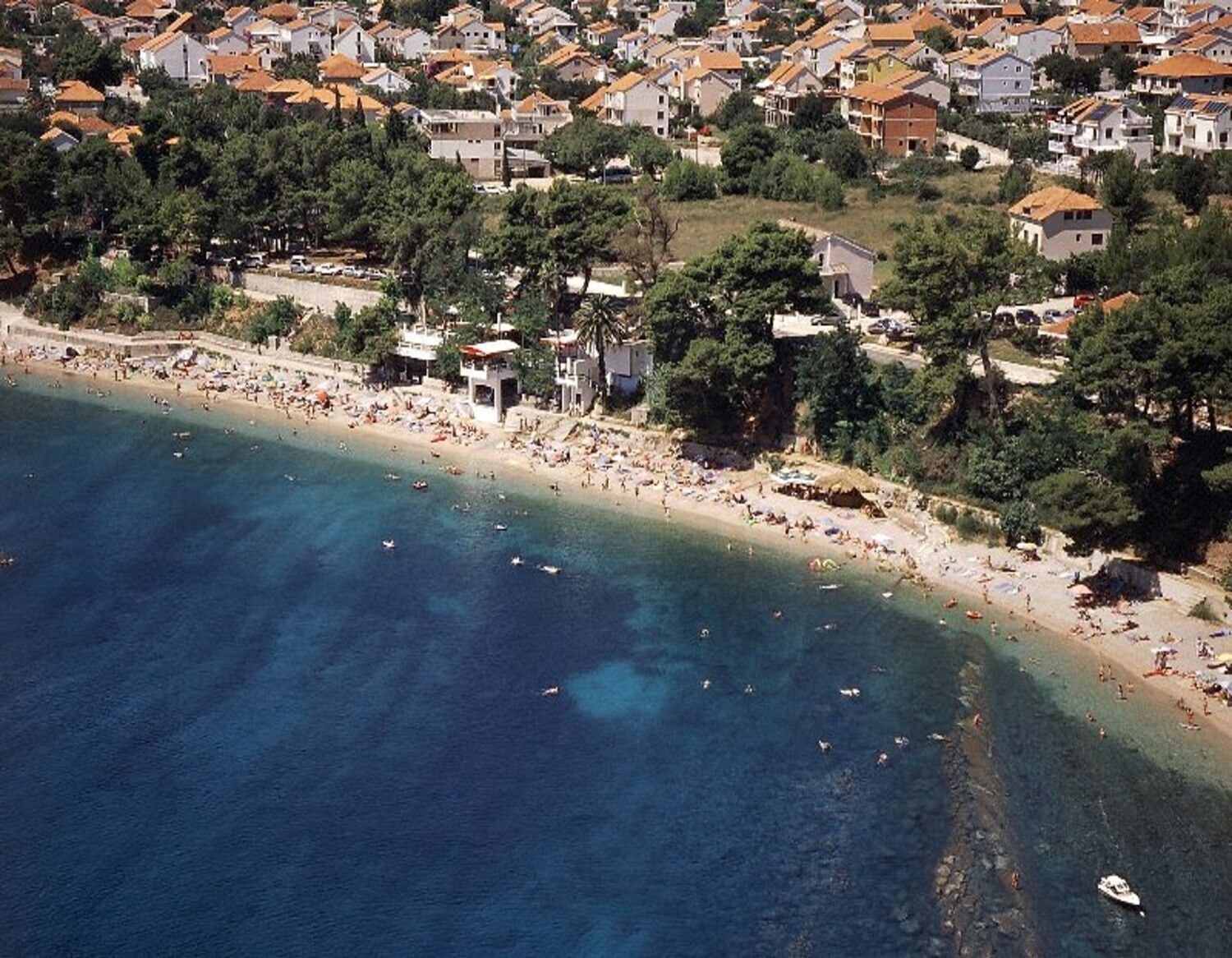 An aerial view of a coastal town with a beach, houses, and clear blue waters.
