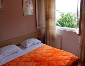 A bedroom with a bed, a window with curtains, and a view of greenery outside. - Apartments Boris (Orebic)