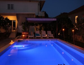 A swimming pool with a blue light, lounge chairs, and a covered area with stairs leading to a door. - Apartments Boris (Orebic)