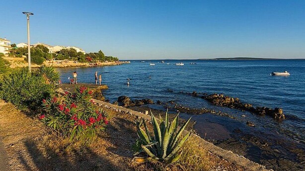 A coastal scene with a rocky shoreline, a clear blue sky, and a few boats on the water. - Apartment Uga2 (Kolan)