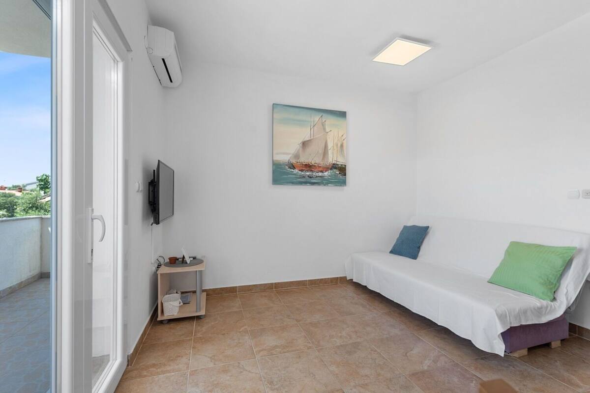 A small, bright room with a white sofa, a painting of a sailboat, a television, and a small table with a plant.