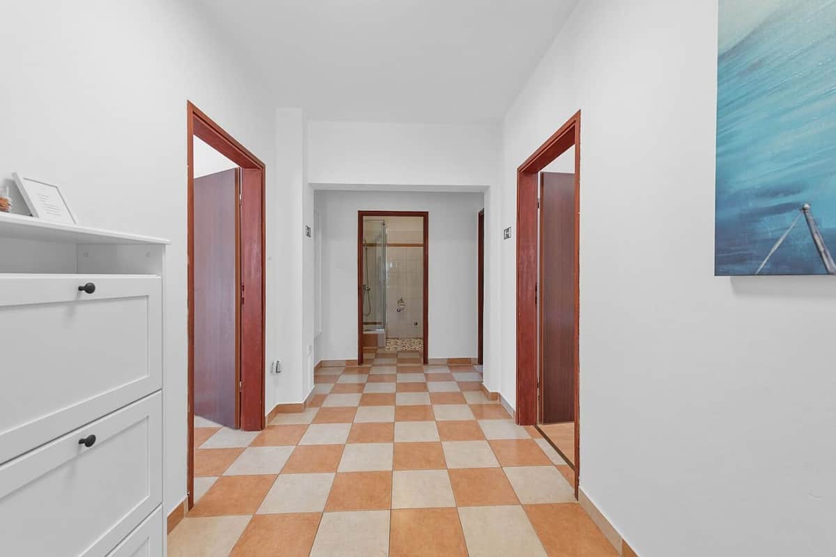 A hallway with checkered flooring, white walls, and wooden doors leading to rooms.