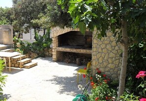 A stone-built outdoor kitchen area with a pizza oven, surrounded by steps, a yellow chair, and various plants. - Apartments Bari (Kolan)