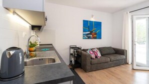 A modern kitchen with a kettle, a sink, and a countertop. There is a gray sofa and a colorful painting on the wall. - Apartments Bari (Kolan)