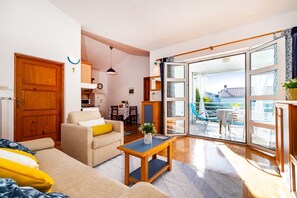 A cozy living room with a sofa, a coffee table, and a dining area. There is a sliding glass door leading to an outdoor patio. - Apartments Bari (Kolan)