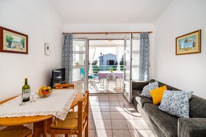 Een kamer met een eettafel, stoelen, een bank en een televisie. Er is een balkon met een tafel en stoelen.