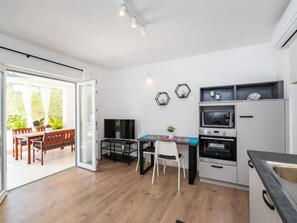 A modern kitchen with a dining area, a TV, and a sliding glass door leading to an outdoor patio. - Apartments Bari (Kolan)