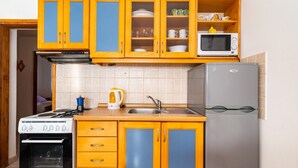 A compact kitchen with yellow cabinets, a stove, a microwave, and a refrigerator. - Apartments Bari (Kolan)