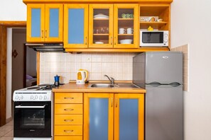 A compact kitchen with yellow cabinets, a stove, a microwave, and a refrigerator. - Apartments Bari (Kolan)