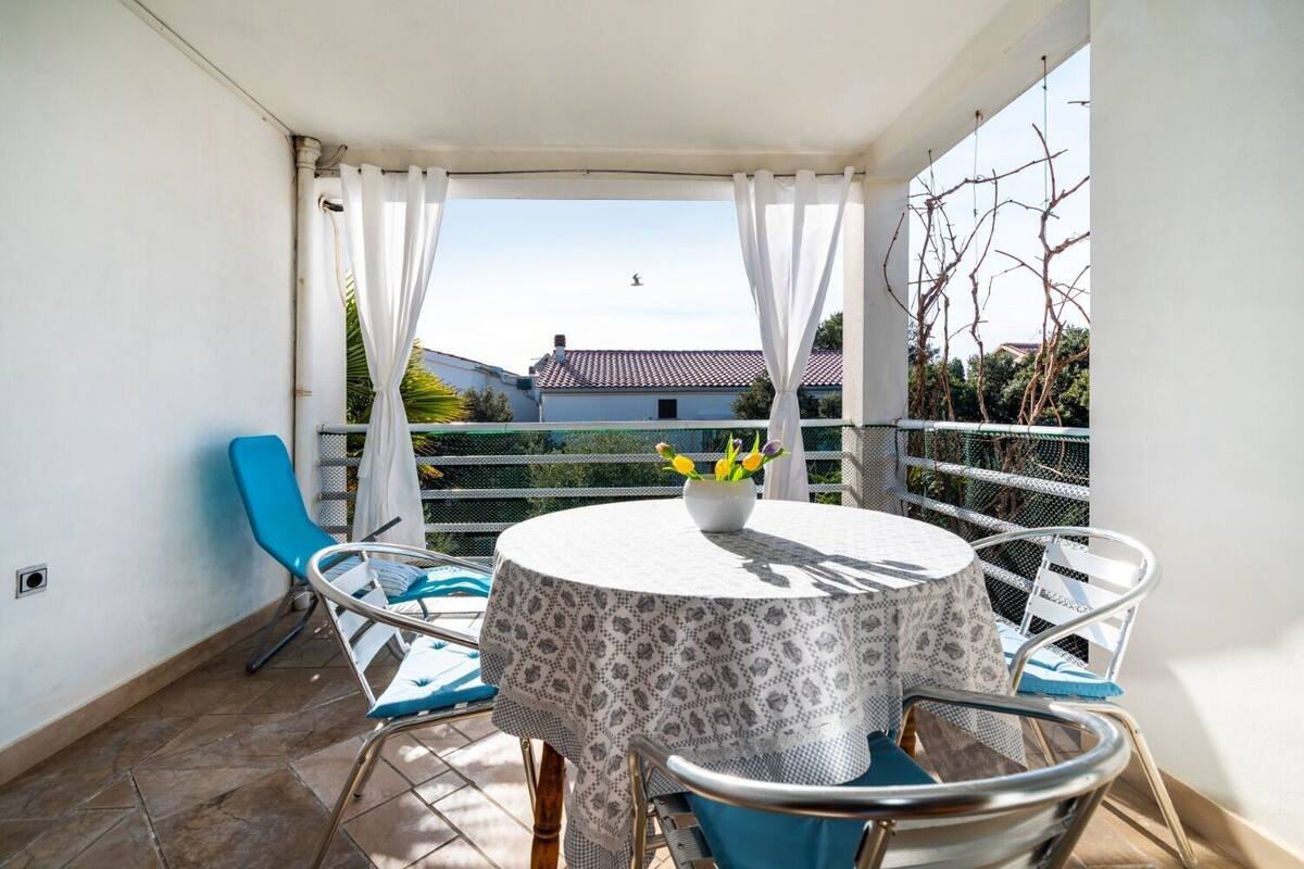 Un balcon avec une table ronde, des chaises bleues et un vase rempli de fleurs.