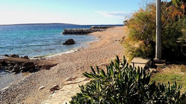 A pebble beach with a rocky breakwater, a clear sky, and some vegetation. - Apartments Bari (Kolan)