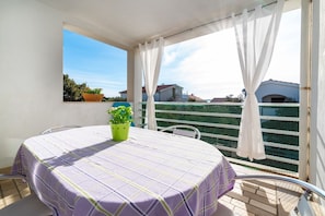 A balcony with a table and chairs, a potted plant, and a view of buildings. - Apartments Bari (Kolan)