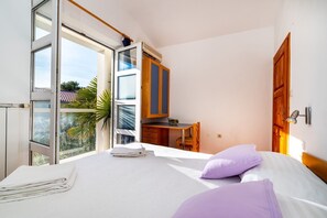 Een slaapkamer met een bed, een bureau en een raam met uitzicht op palmbomen.