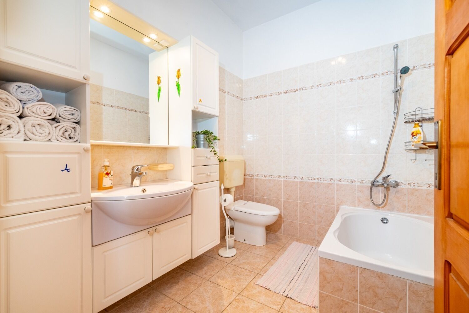 Et badeværelse med vask, toilet og badekar. Der er håndklæder stablet i et skab.