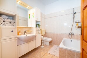 Een badkamer met een wastafel, toilet en bad. Handdoeken liggen opgestapeld in een kast.