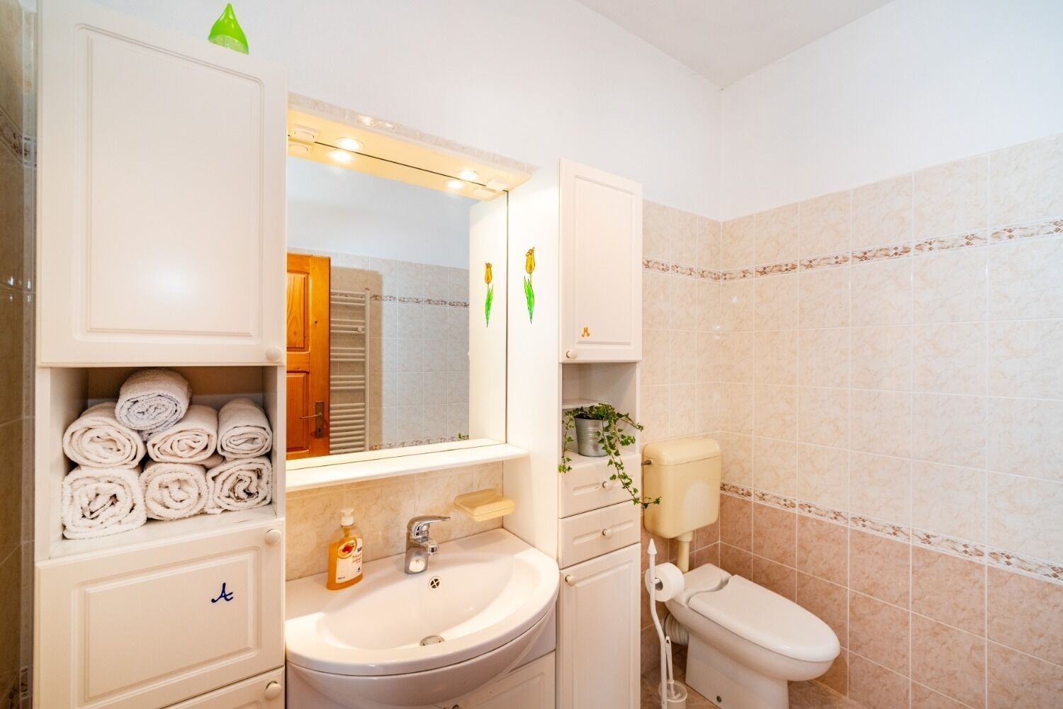 Casa de banho com lavatório, espelho, sanita e espaço para toalhas.