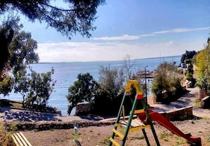 Un parque infantil con un tobogán, un muro de piedra y vistas al mar.