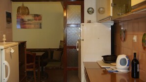 A compact kitchen with a refrigerator, a microwave, and a kettle on the counter. There's a dining area with a table and chairs visible through a doorway. - Apartments Sonja (Podgora)