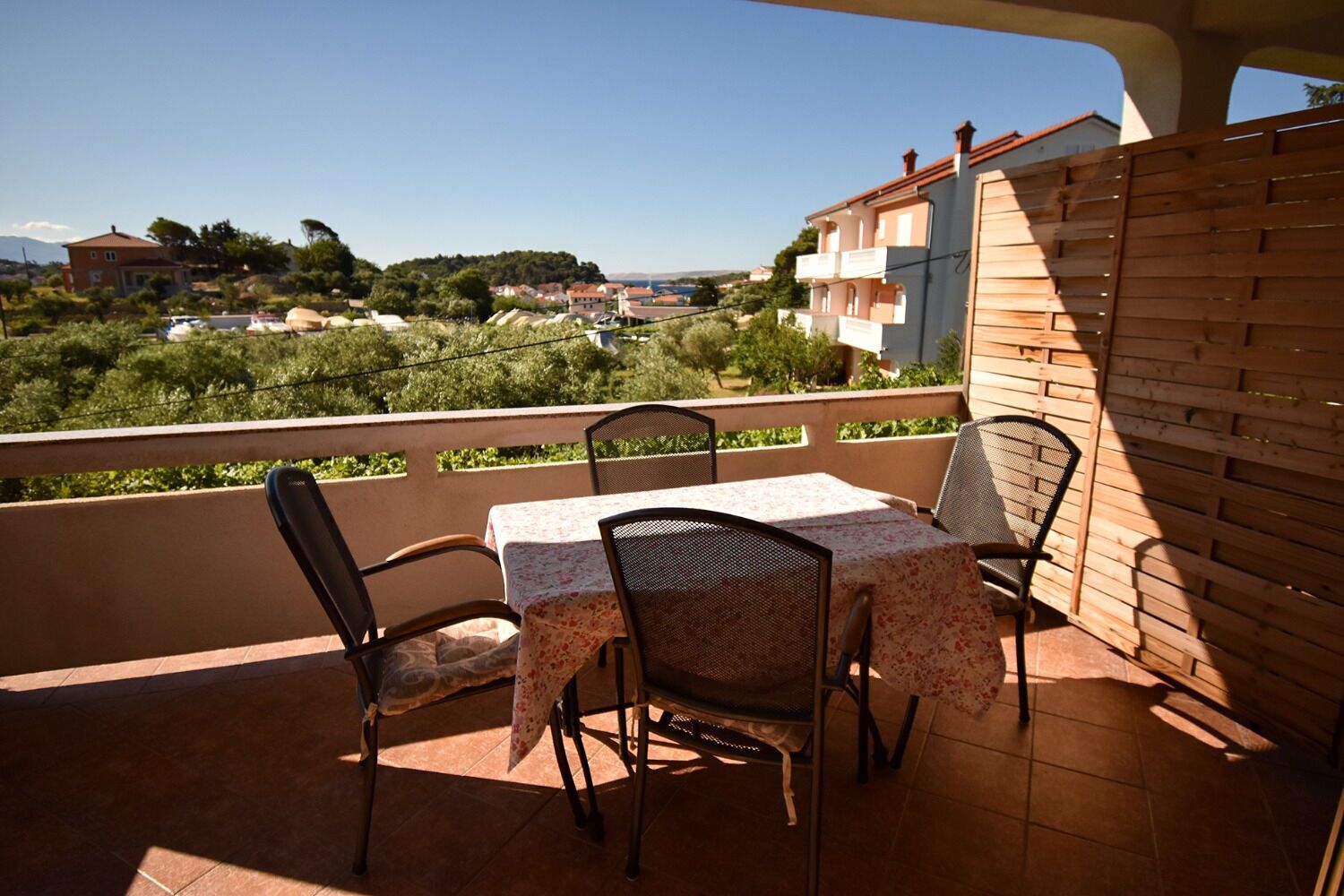 A balcony with a table and chairs, overlooking a residential area with houses and greenery.
