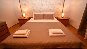 A neatly made bed with two pillows, two bedside tables with lamps, and a wooden dresser. - Apartments and Rooms Frane (Rab)