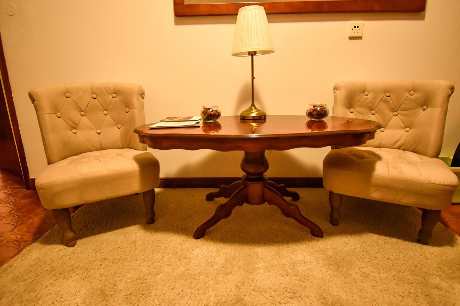 A room with a round wooden table, two upholstered chairs, a lamp, and a small decorative item on the table.