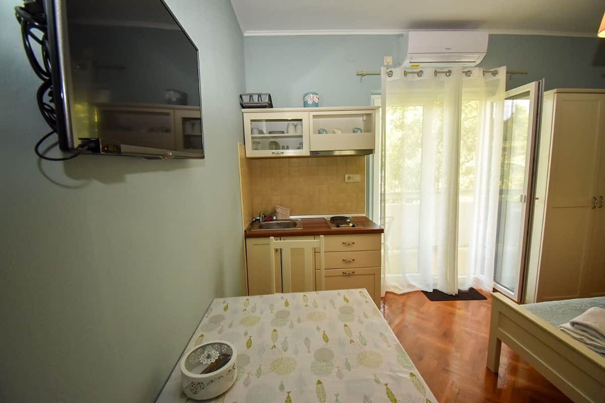A compact room with a kitchenette, a bed, and a window with curtains.