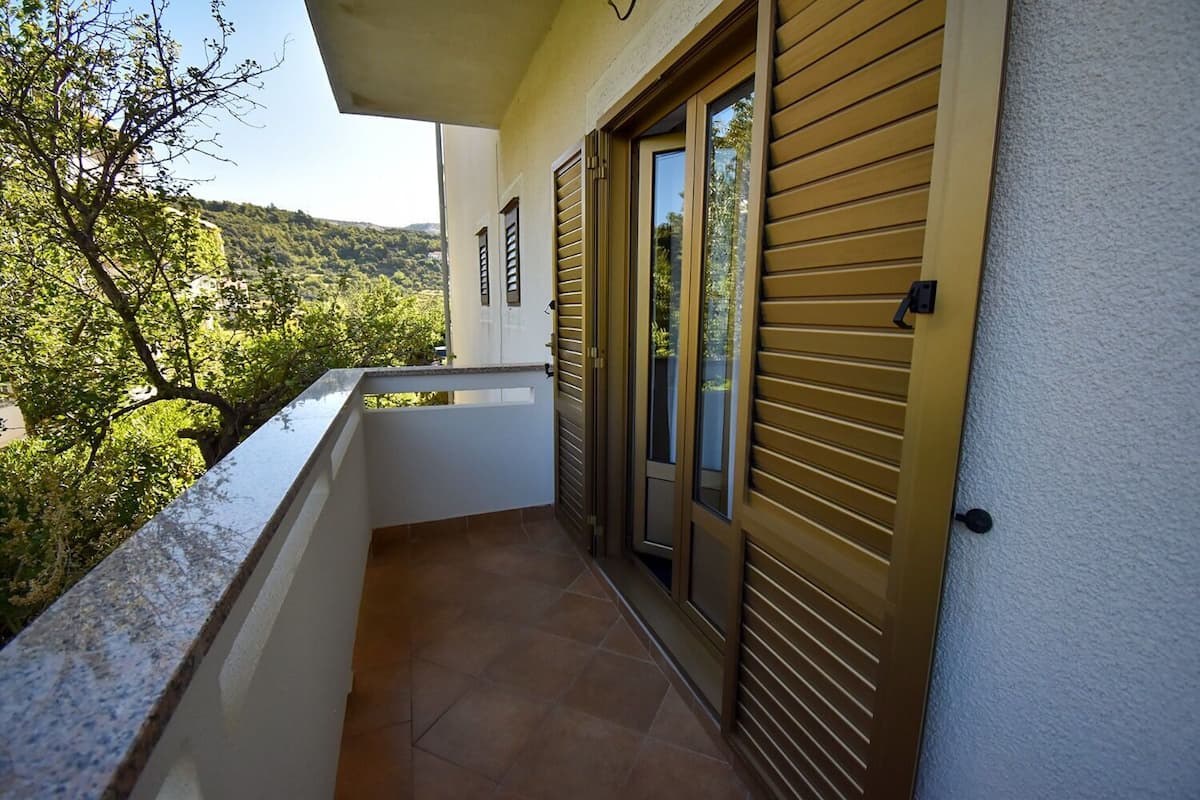 A balcony with a view of a hillside, a sliding glass door, and a tiled floor.