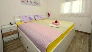 Un dormitorio con cama, mesita de noche, ventana con cortinas y un cuadro floral en la pared.