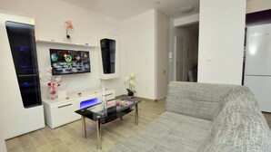 Una sala de estar moderna con un sofá gris, una mesa de centro de vidrio, un televisor de pantalla plana y un aparador blanco.