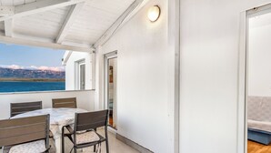 Un porche cubierto con una mesa y sillas, vista al mar y una puerta que da a un espacio interior.