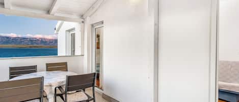 Um alpendre coberto com mesa e cadeiras, vista para o mar e porta que dá para um espaço interno.