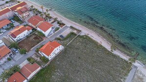 Vista aérea de una zona residencial costera con casas de techo rojo, una playa de arena y mar azul cristalino.