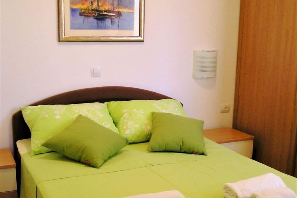 A neatly made bed with green bedding and pillows, a framed painting above it, and a wooden headboard.