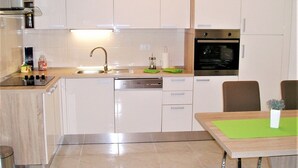 Eine moderne Küche mit weißen Schränken, einem eingebauten Backofen und einer Essecke mit einem grünen Tischläufer.