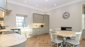 Een moderne keuken met een marmeren aanrecht, een eethoek met een houten tafel en witte stoelen, en een klok aan de muur.