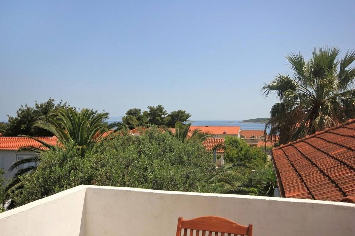 A residential area with red-tiled roofs, palm trees, and a view of the sea.
