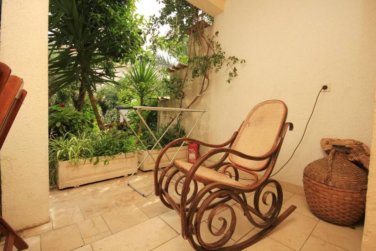 A rocking chair in a patio area with a view of greenery and a small table with a basket.