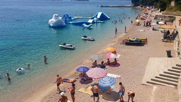 Ein Strand mit aufblasbaren Wasserspielen, blauem Meer und Menschen, die sich sonnen.