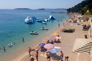 Una playa con juguetes inflables, un mar azul cristalino y gente tomando el sol.
