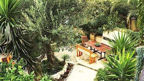 Ein Patio mit Holztisch und -stühlen, umgeben von üppigem Grün und einer Steinsäule.