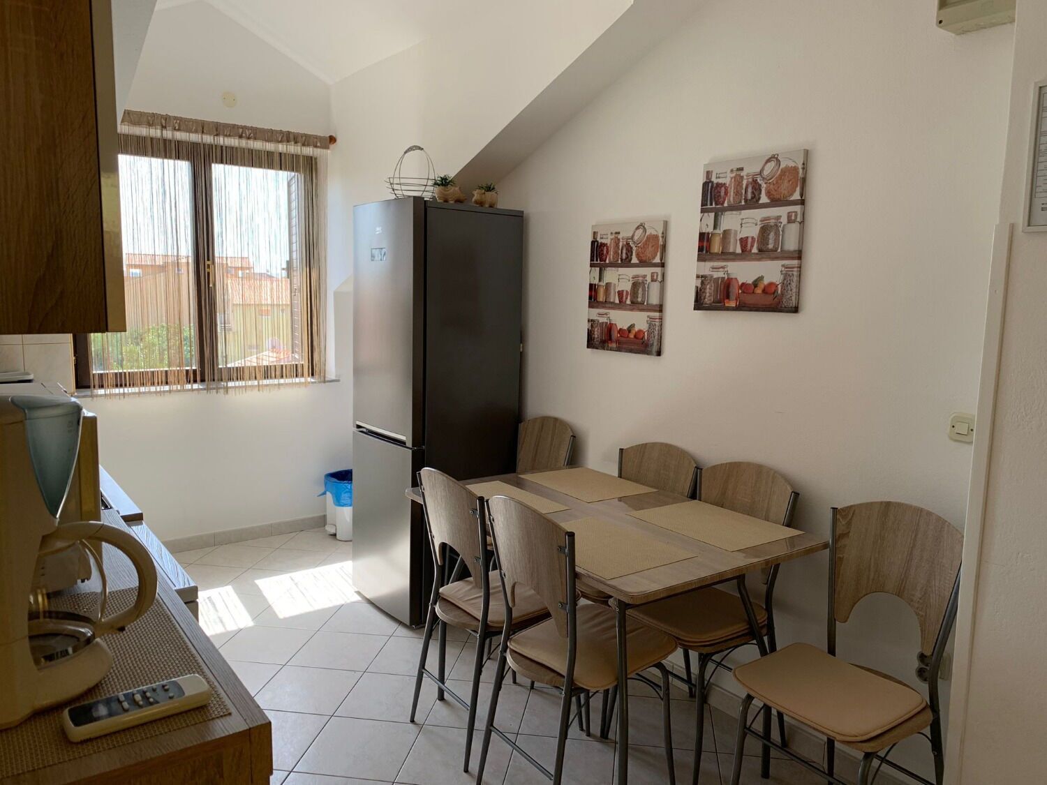 A compact kitchen with a dining table, chairs, a refrigerator, and a coffee machine.