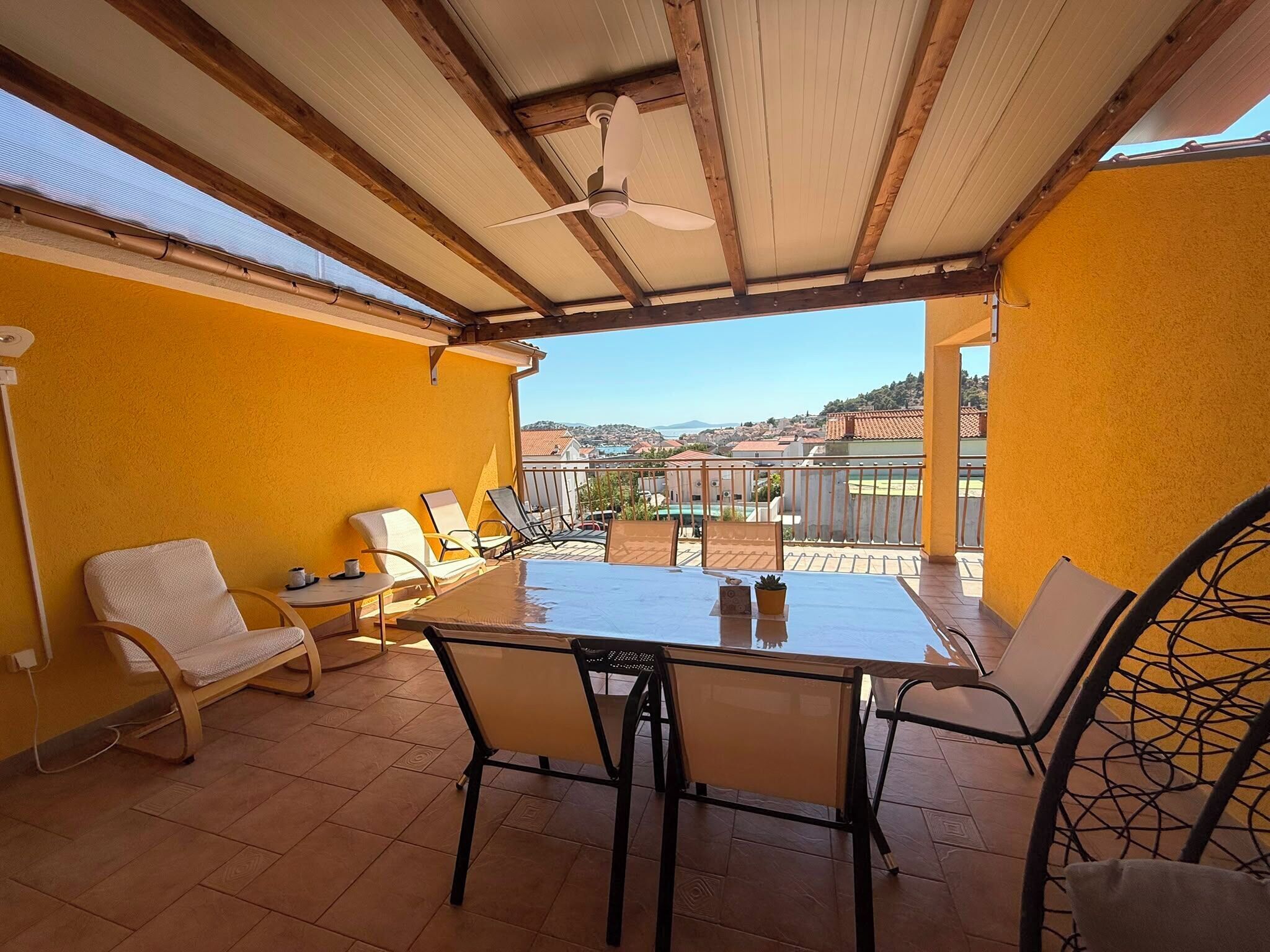 A covered outdoor patio with a table and chairs, a ceiling fan, and a view of the surrounding area.