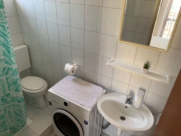 A compact bathroom with a toilet, washing machine, and sink. - Apartment Ivica (Tribunj)