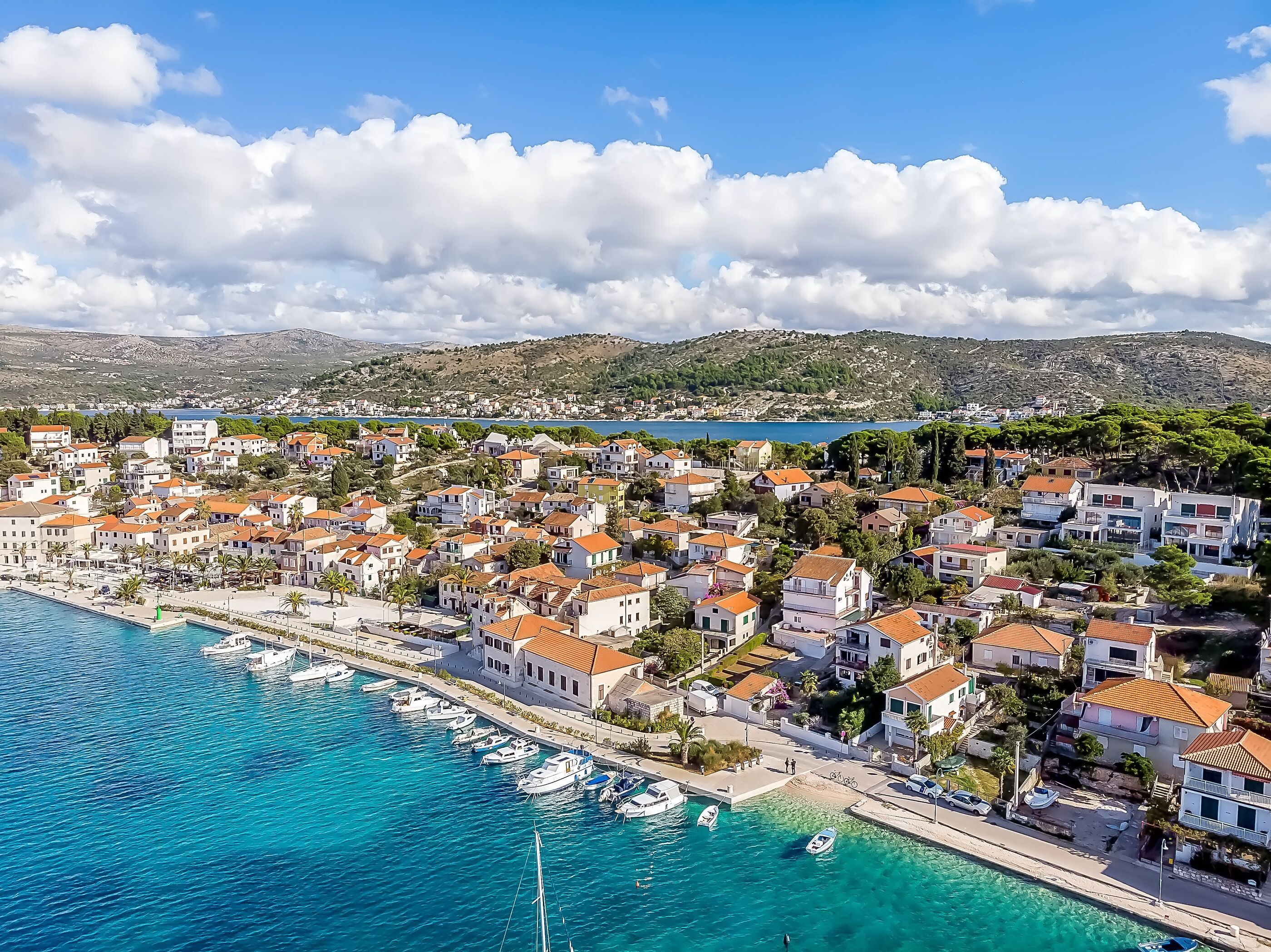 A coastal town with a marina, buildings with red-tiled roofs, and a clear blue sky.