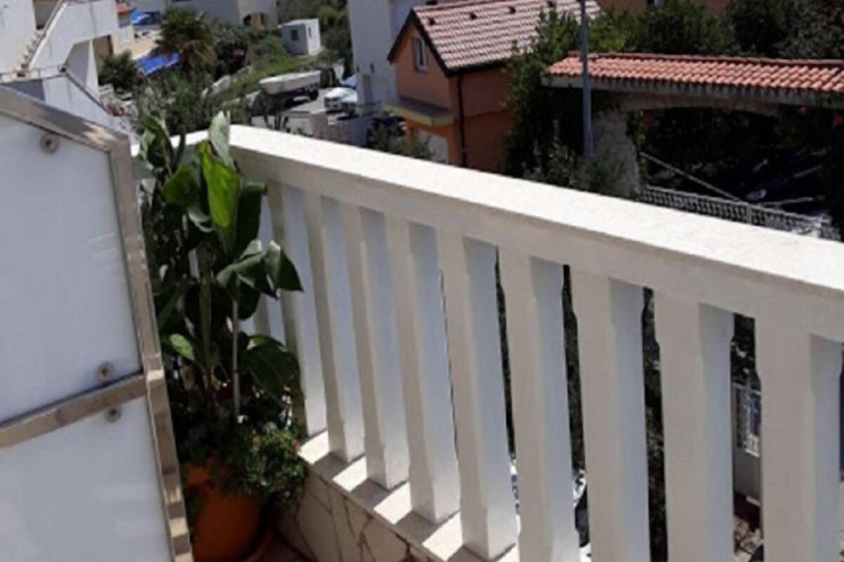 A residential area with houses, a white balcony with a railing, and a potted plant.