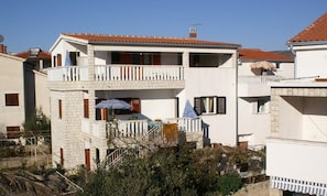A two-story residential building with a balcony, a chimney, and a small garden area. - Apartments Amalija (Rogoznica)