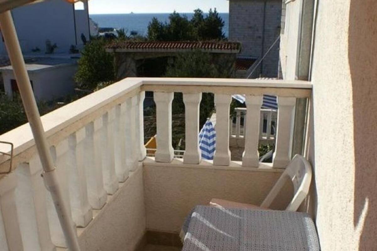 A balcony with two chairs, a mop, and a striped umbrella.