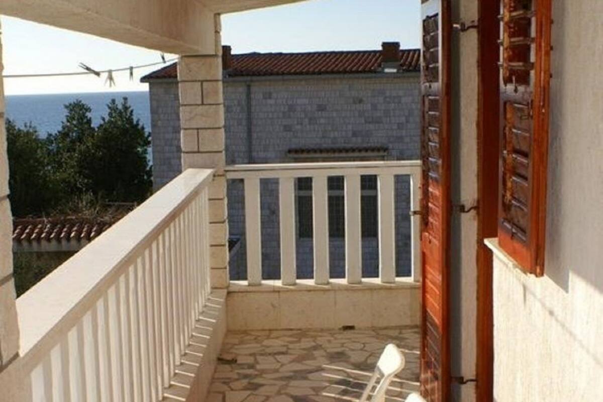 A balcony with stone flooring, white railings, and two white lounge chairs.