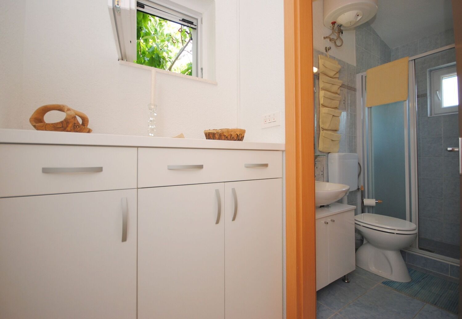 A bathroom with a toilet, a sink, and a shower. There is a window above the sink and a towel rack above the toilet.