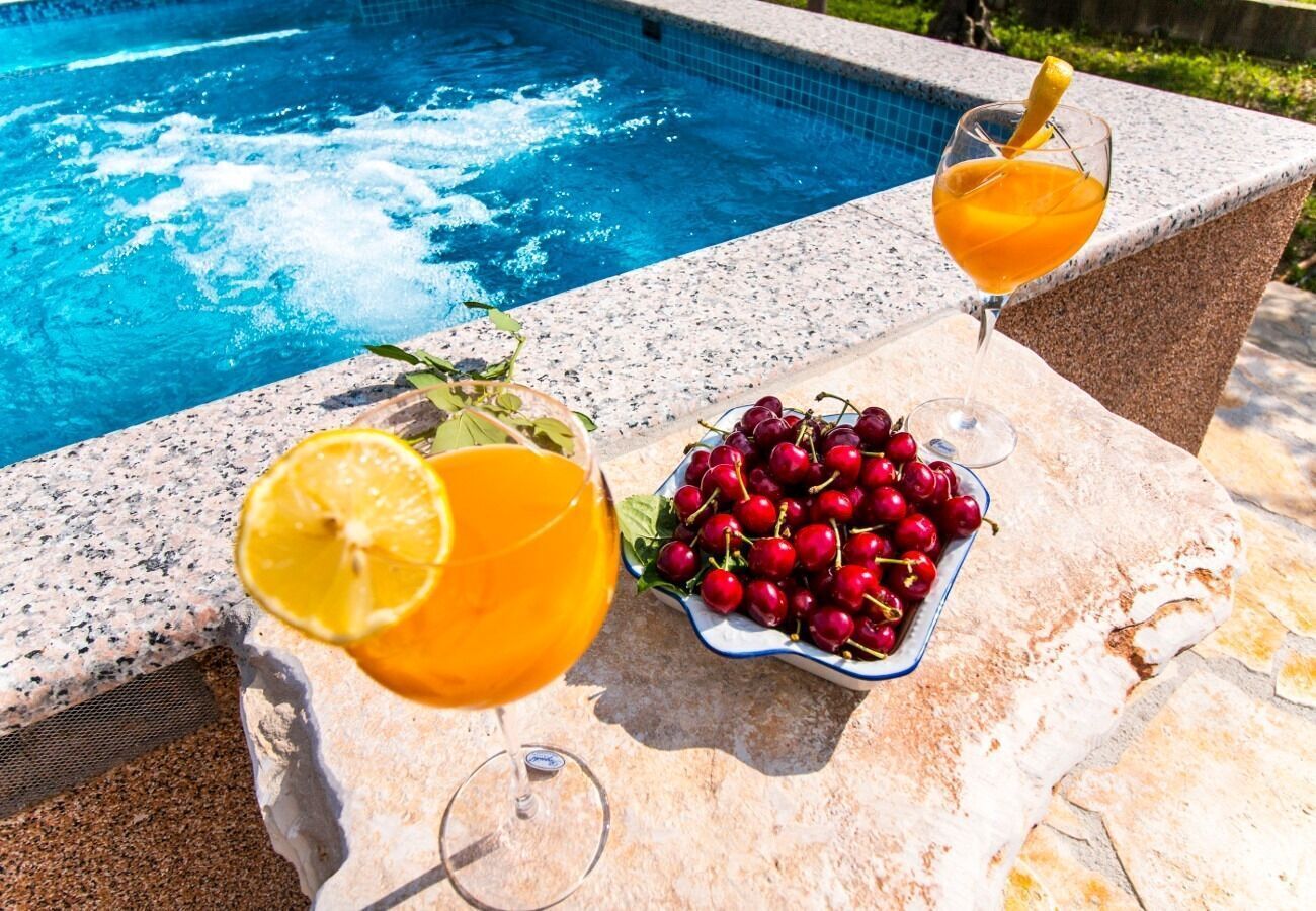 A poolside table with two glasses of orange juice, a bowl of cherries, and a glass of orange juice with a lemon slice.